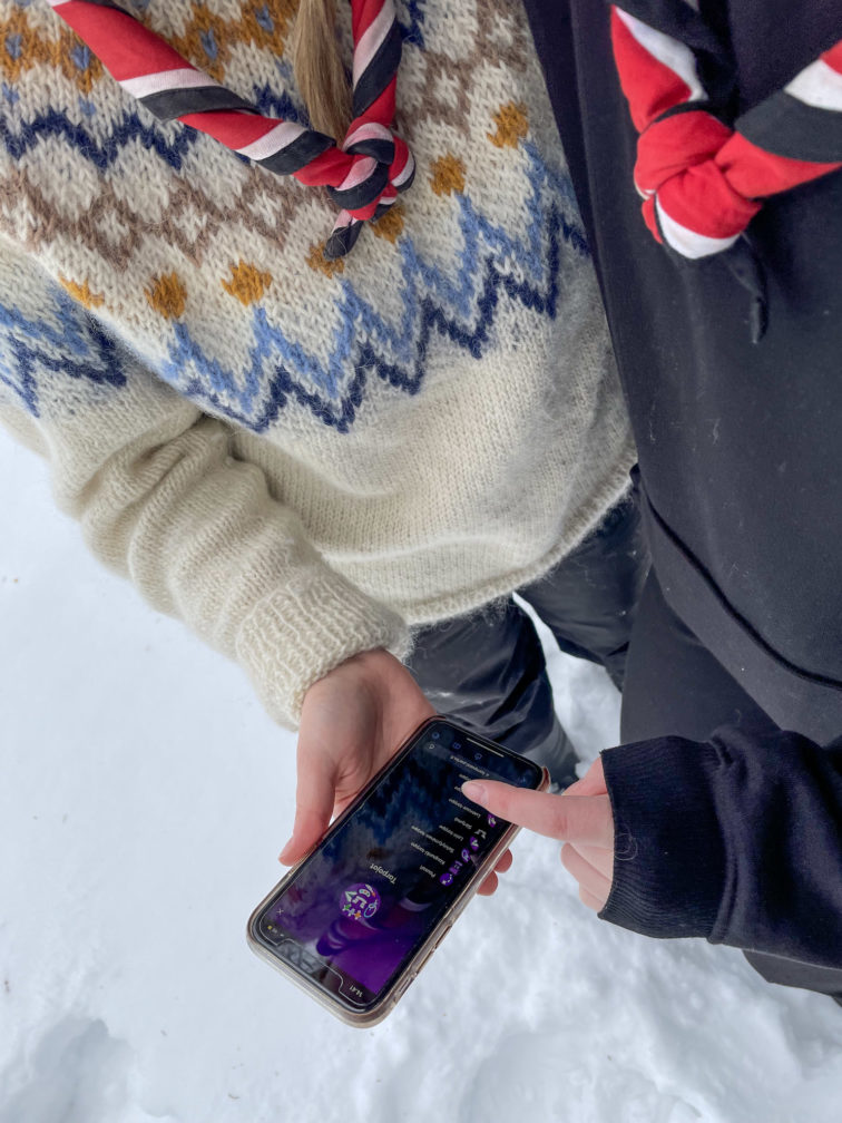 Kaksi partiolaista seisovat vierekkäin lumessa. Toisella on kädessään puhelin, jossa on auki Kompassi-sovelluksen tarpojanäkymä.
